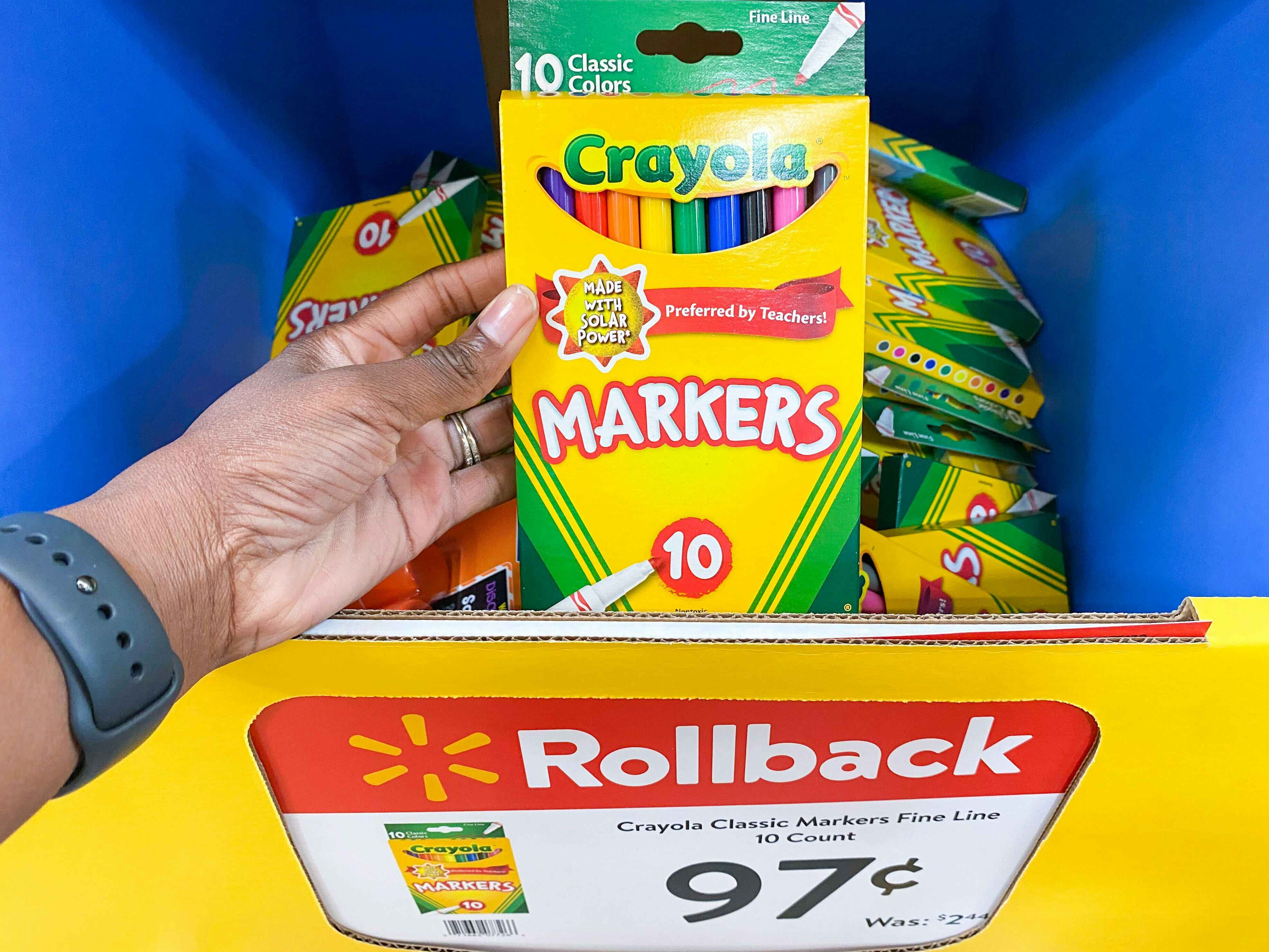 A person's hand holding a box of Crayola markers above a bin of them with a sale sign showing them to be 97 cents each.