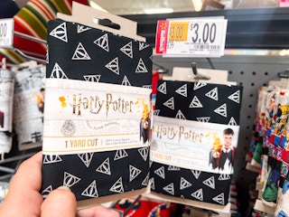 Hand holding Harry Potter printed quilting fabric in front of shelf at Walmart. Price tag indicates that the product is on sale for $3, regularly $6.77.