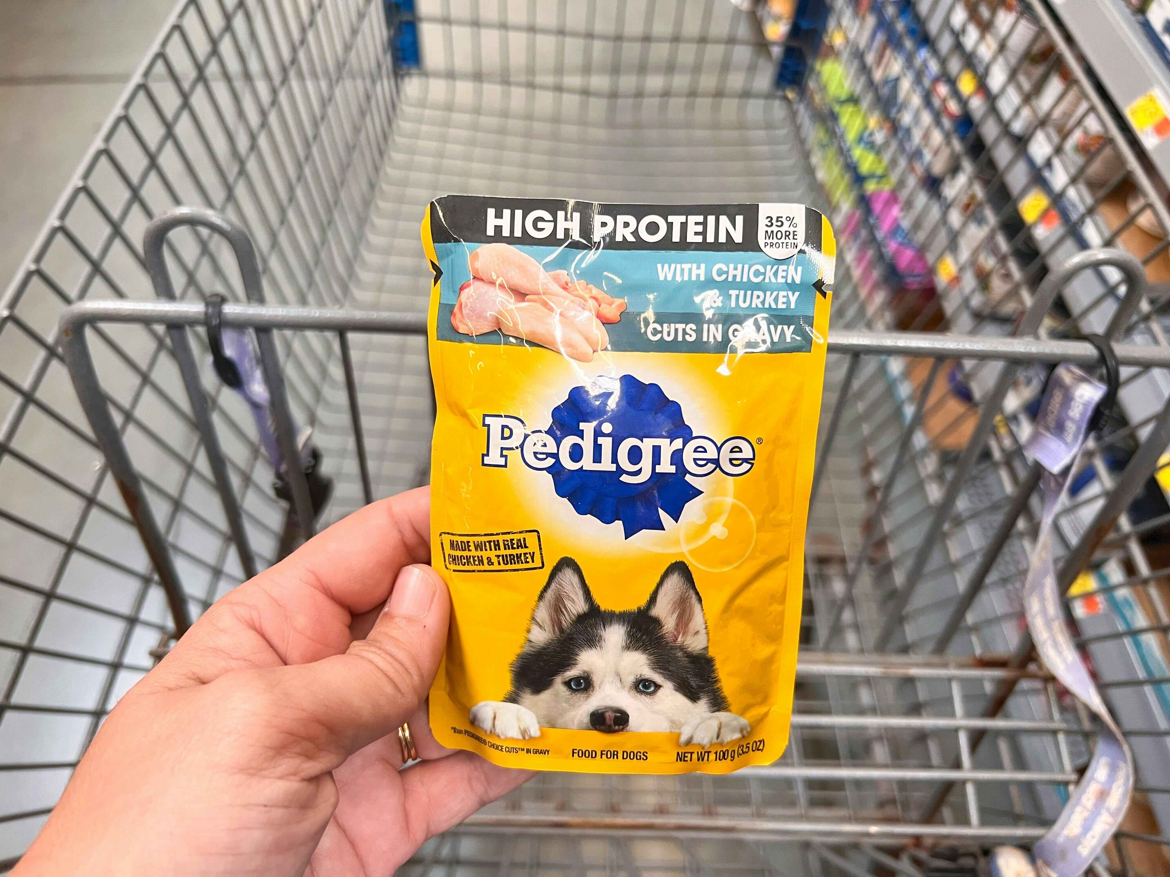 Hand holding one Pedigree High Protein Dog Food Pouch over Walmart shopping cart