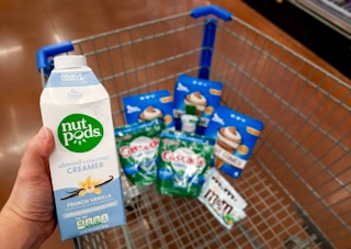 Nutpods Creamer held over Walmart shopping cart full of Blue Bunny, Cascade, and M&M's products