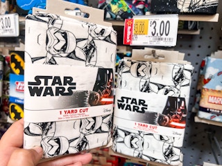Hand holding Star Wars printed quilting fabric in front of shelf at Walmart. Price tag indicates that the product is on sale for $3, regularly $6.77.