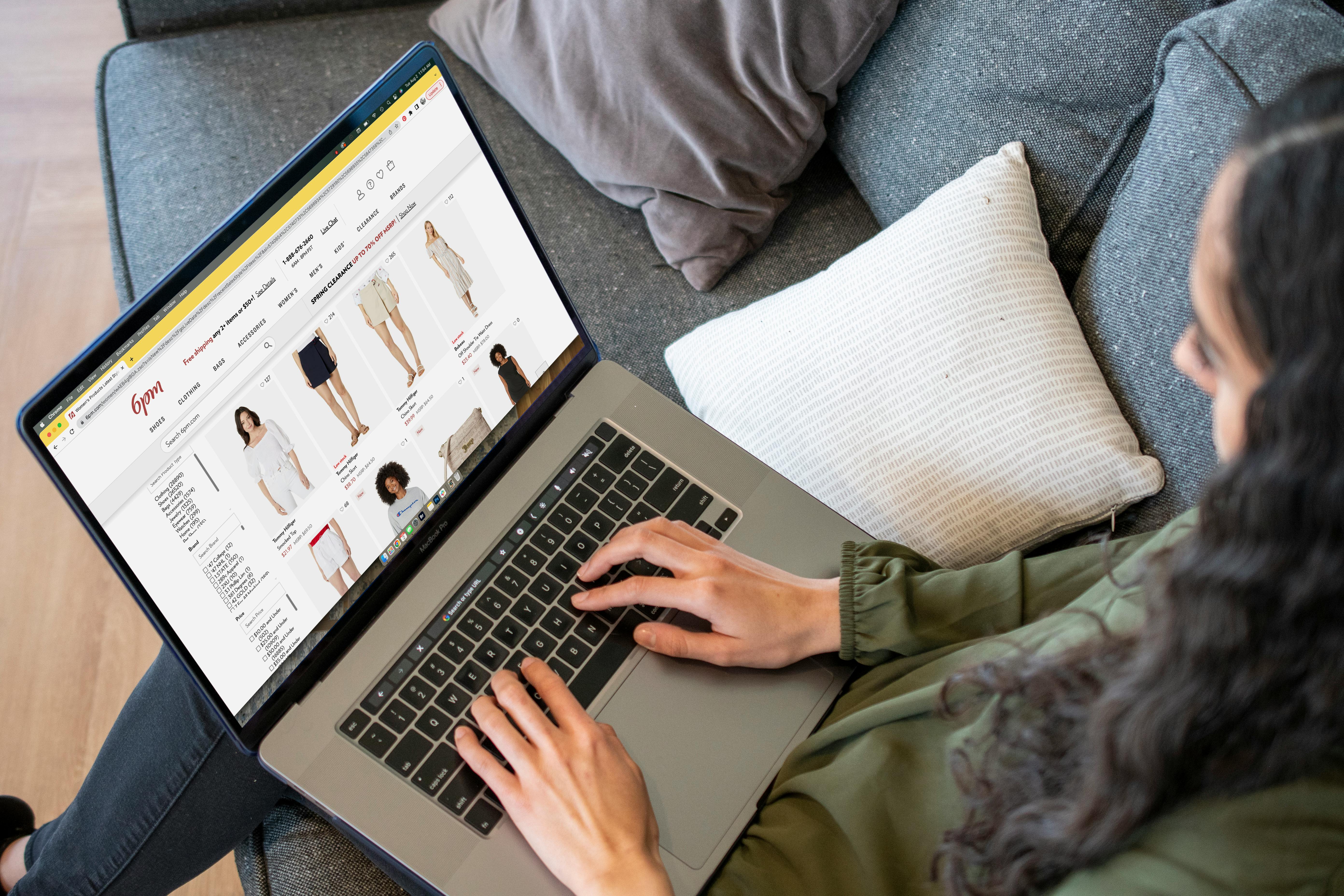 A woman sitting on a sofa with a laptop computer on her lap, looking womens apparel on at 6pm.com.