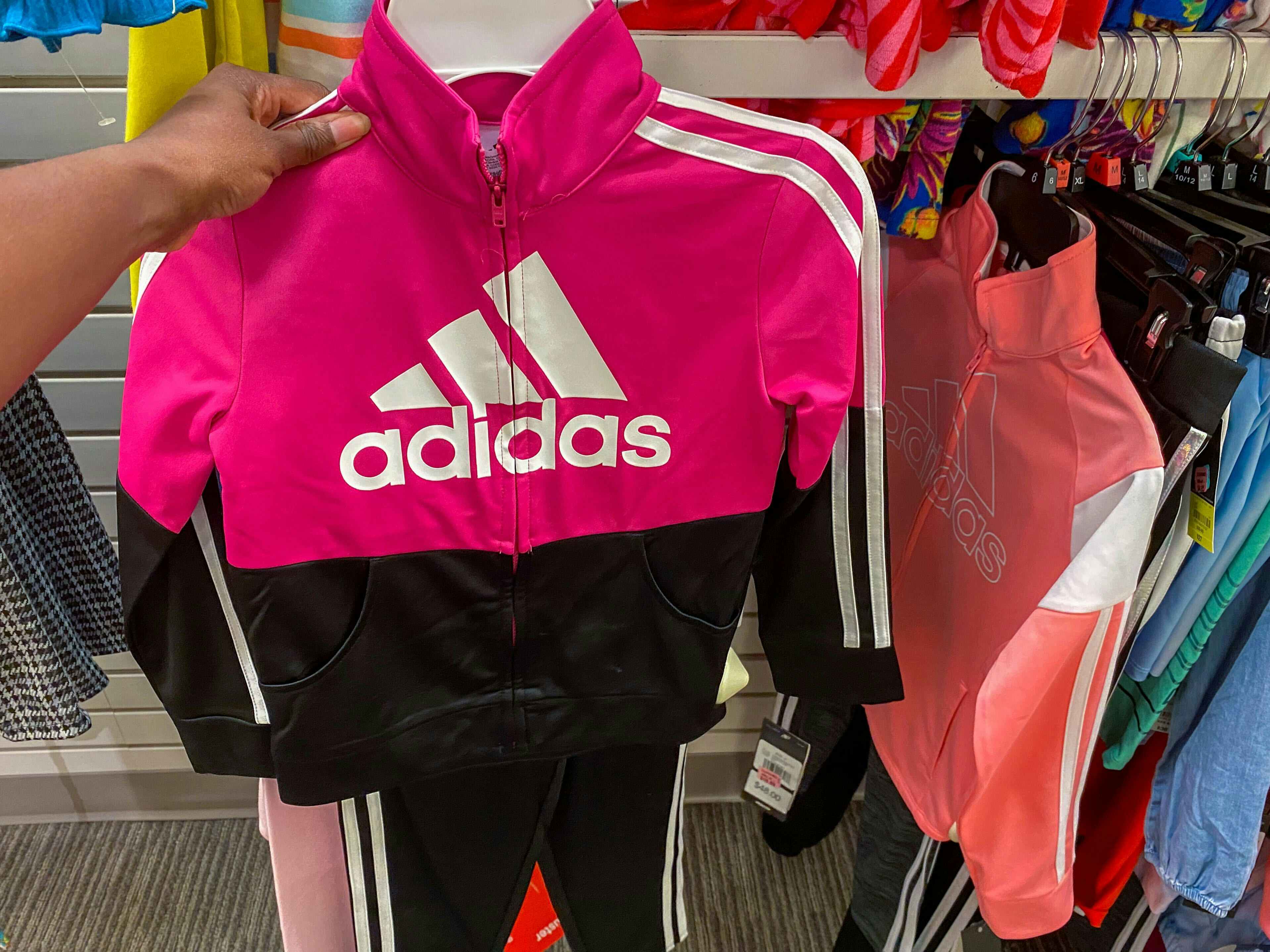 someone holding a pink and black adidas kids outfit