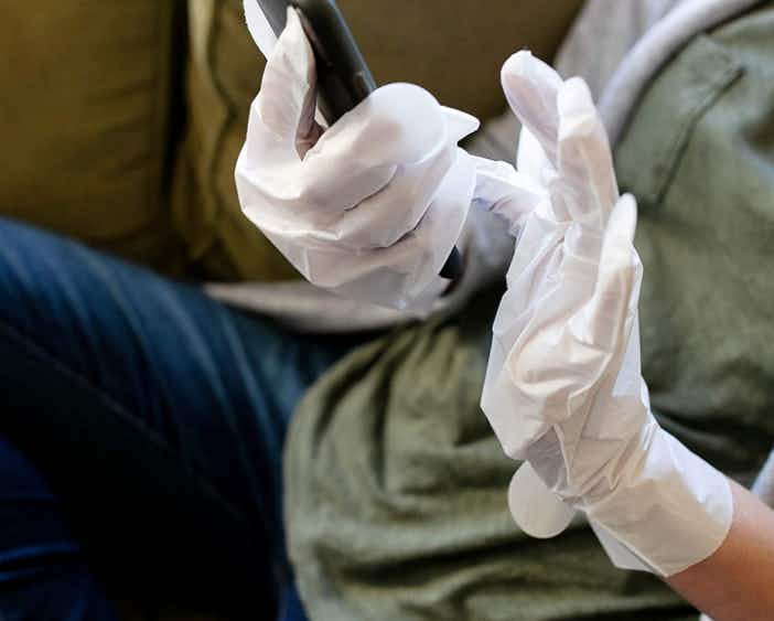 person's hands wearing aveeno gloves and using a smartphone