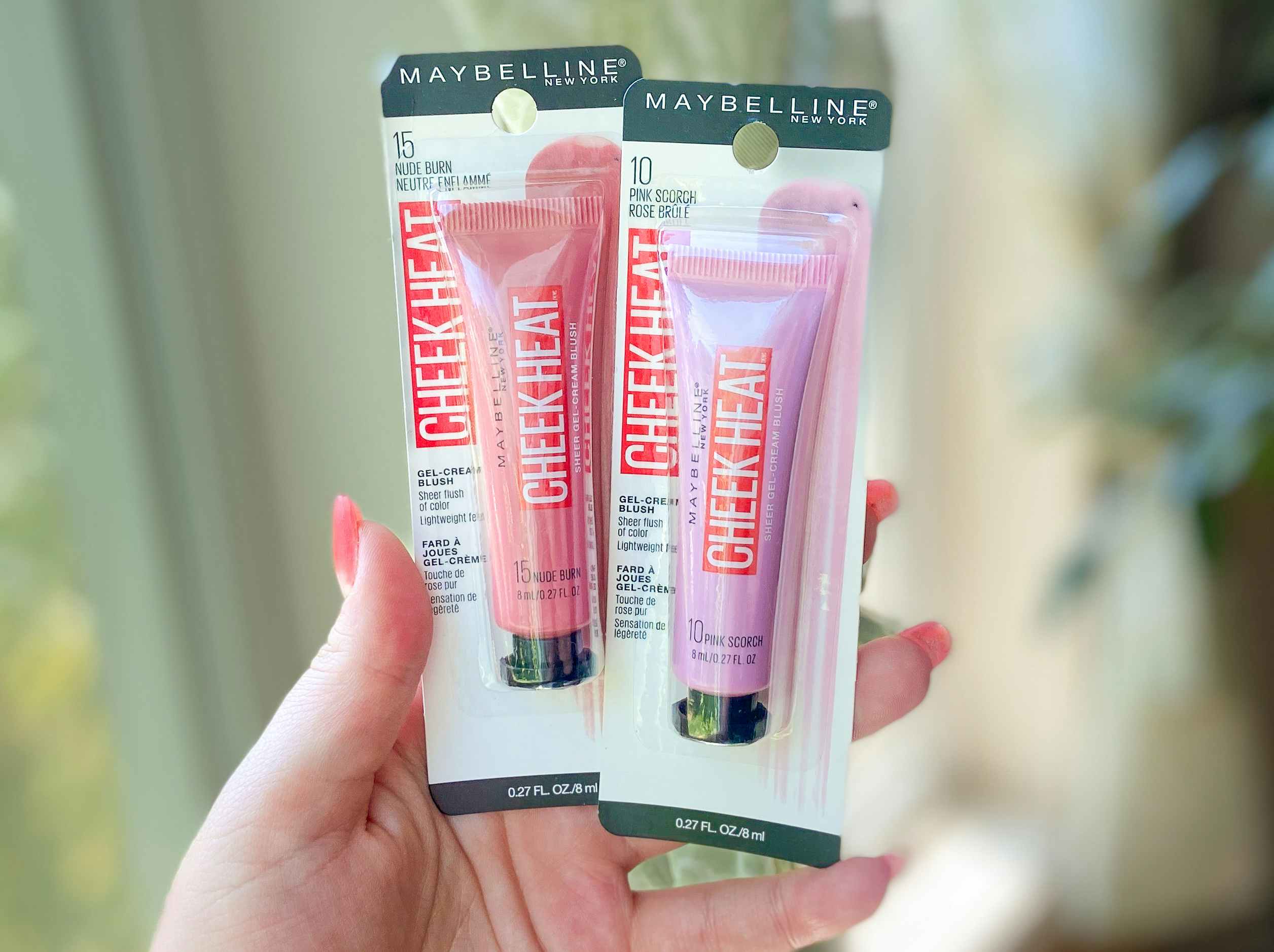 hand holding two maybelline cheek heat cream blush makeup