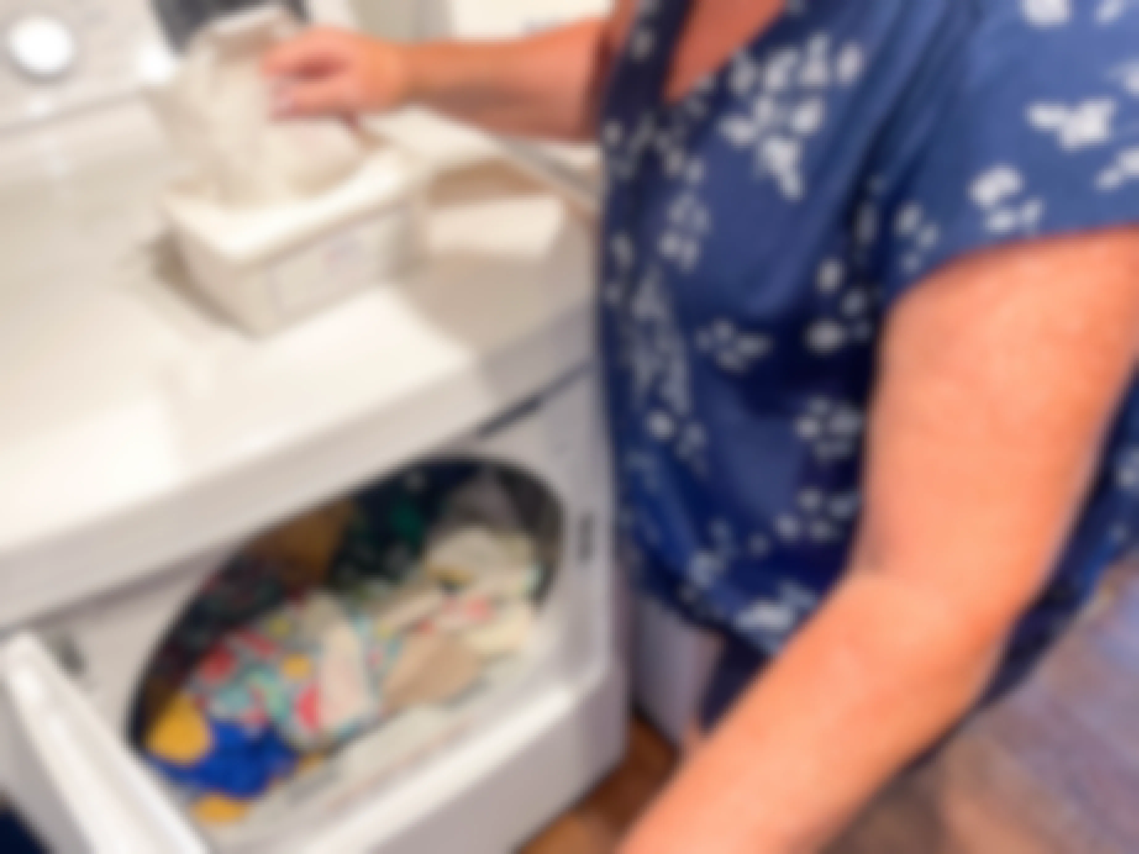 a baby wipe container being reused as a dryer sheet holder with a woman putting a sheet in the dryer