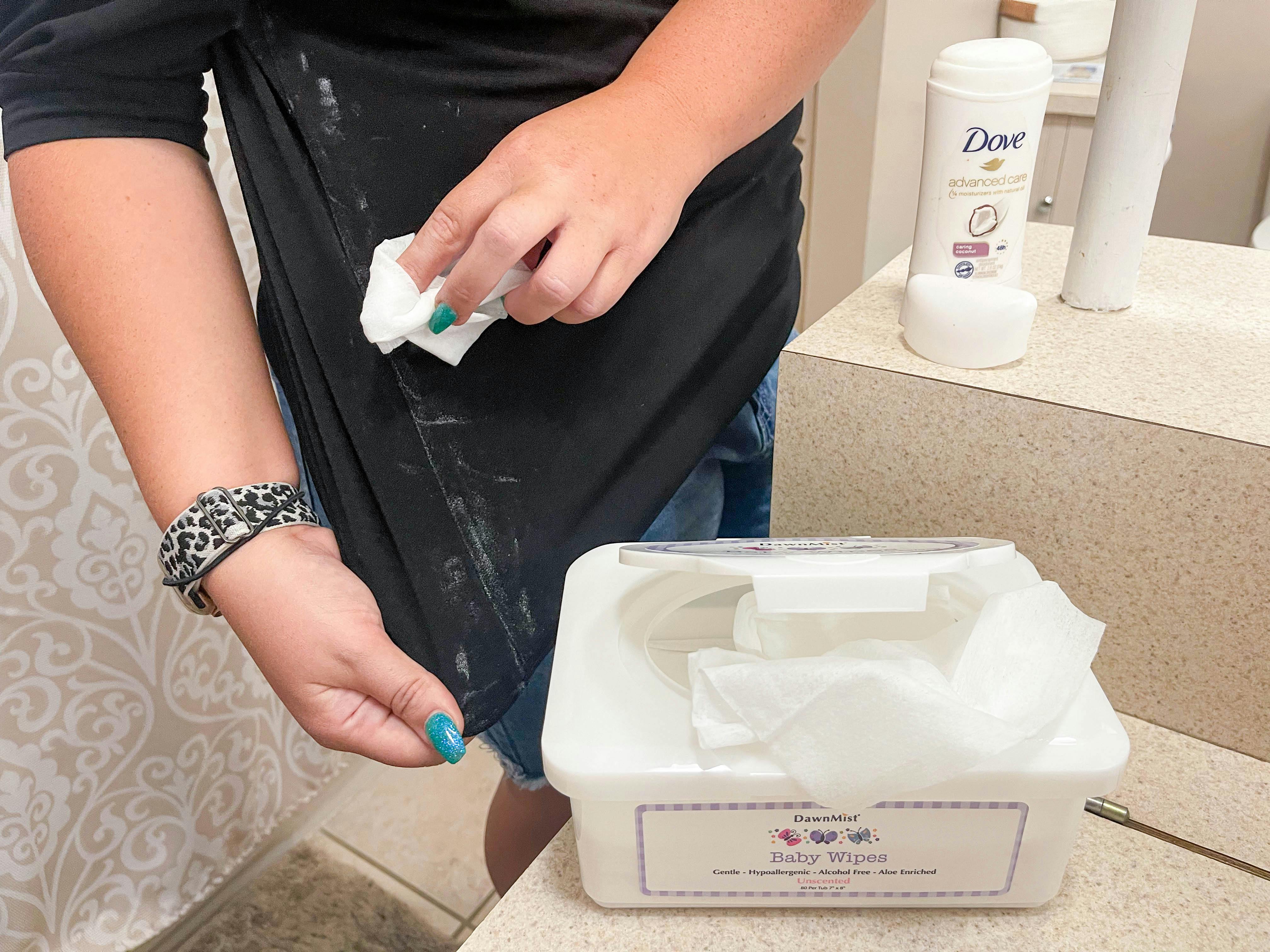 a woman using a baby wipe to wipe up a deodorant stains on shirt