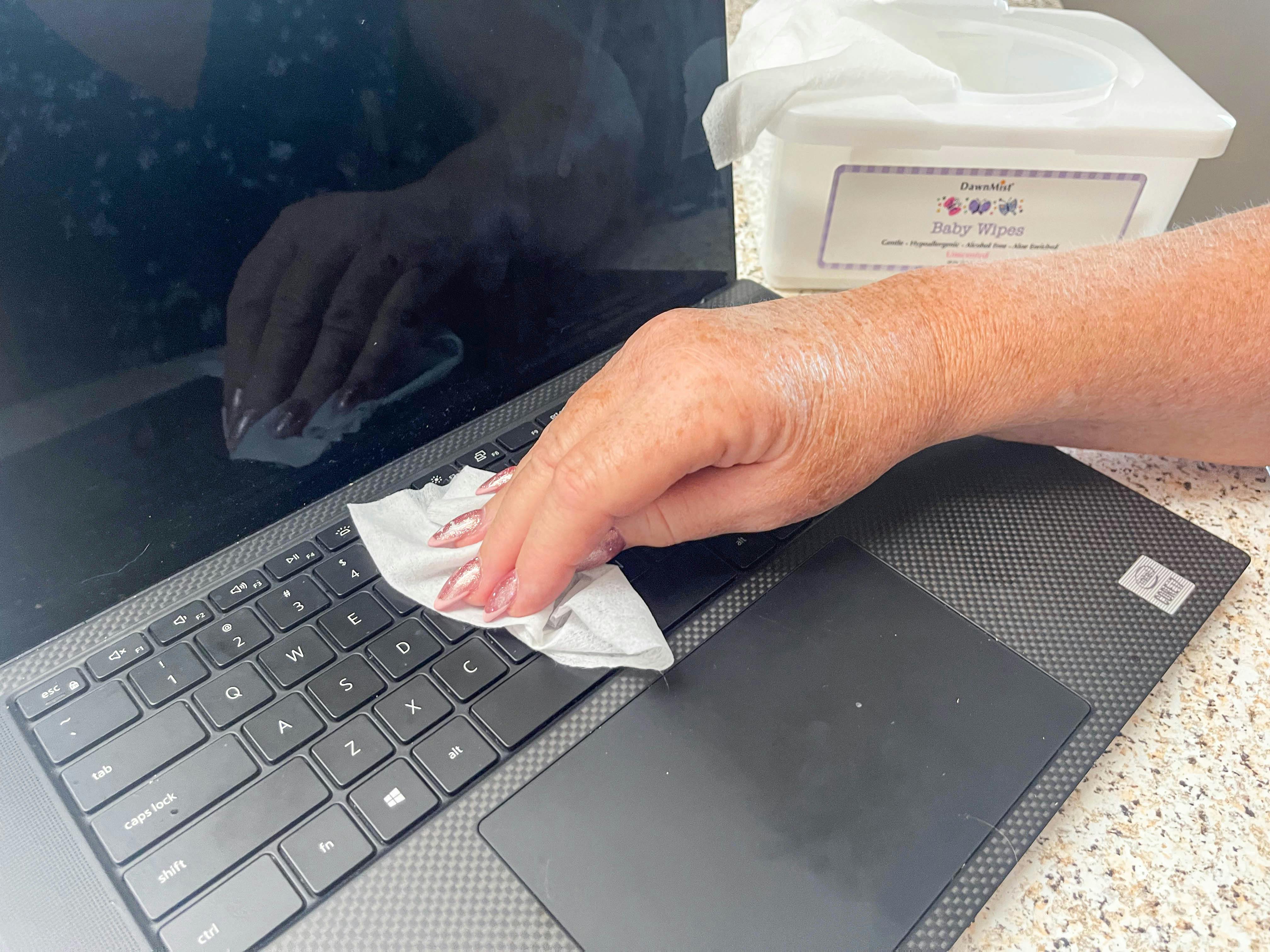 a woman using a baby wipe to wipe up dust on keyboard