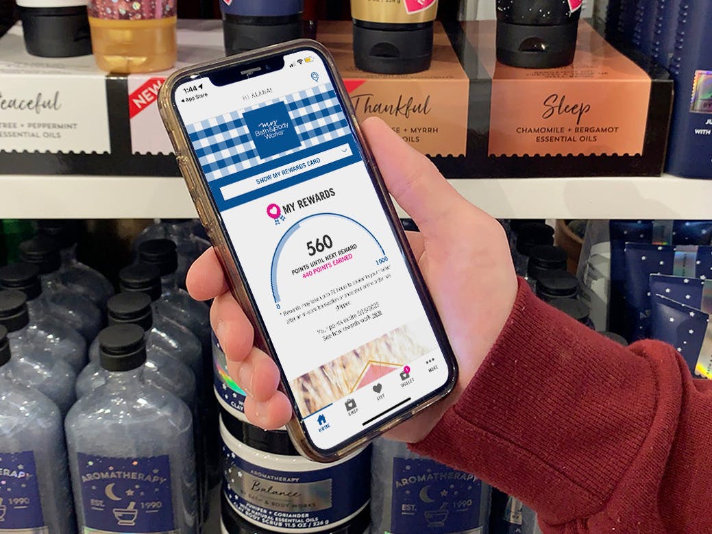 A person holding a cell phone showing the bath and body works reward on the screen, inside a store.