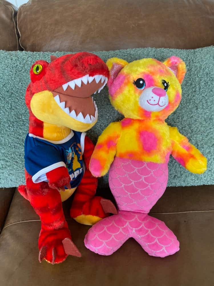 a dinosaur and a kitty-mermaid build-a-bear sitting next to each other