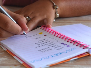 A woman writing a key for a bullet journal in a spiral notebook.