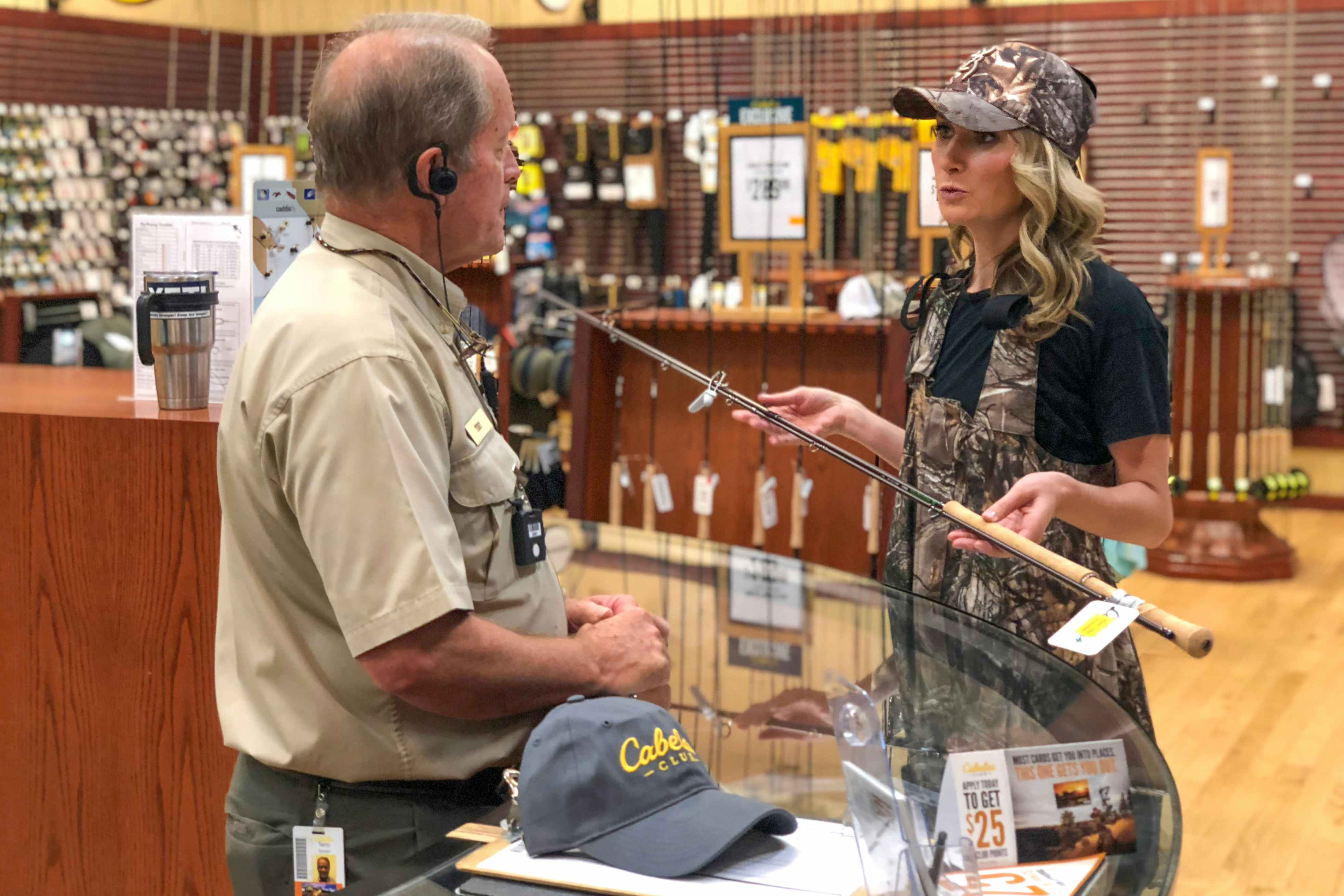 A woman talking to a Cabela's employee while holding a fishing rod.