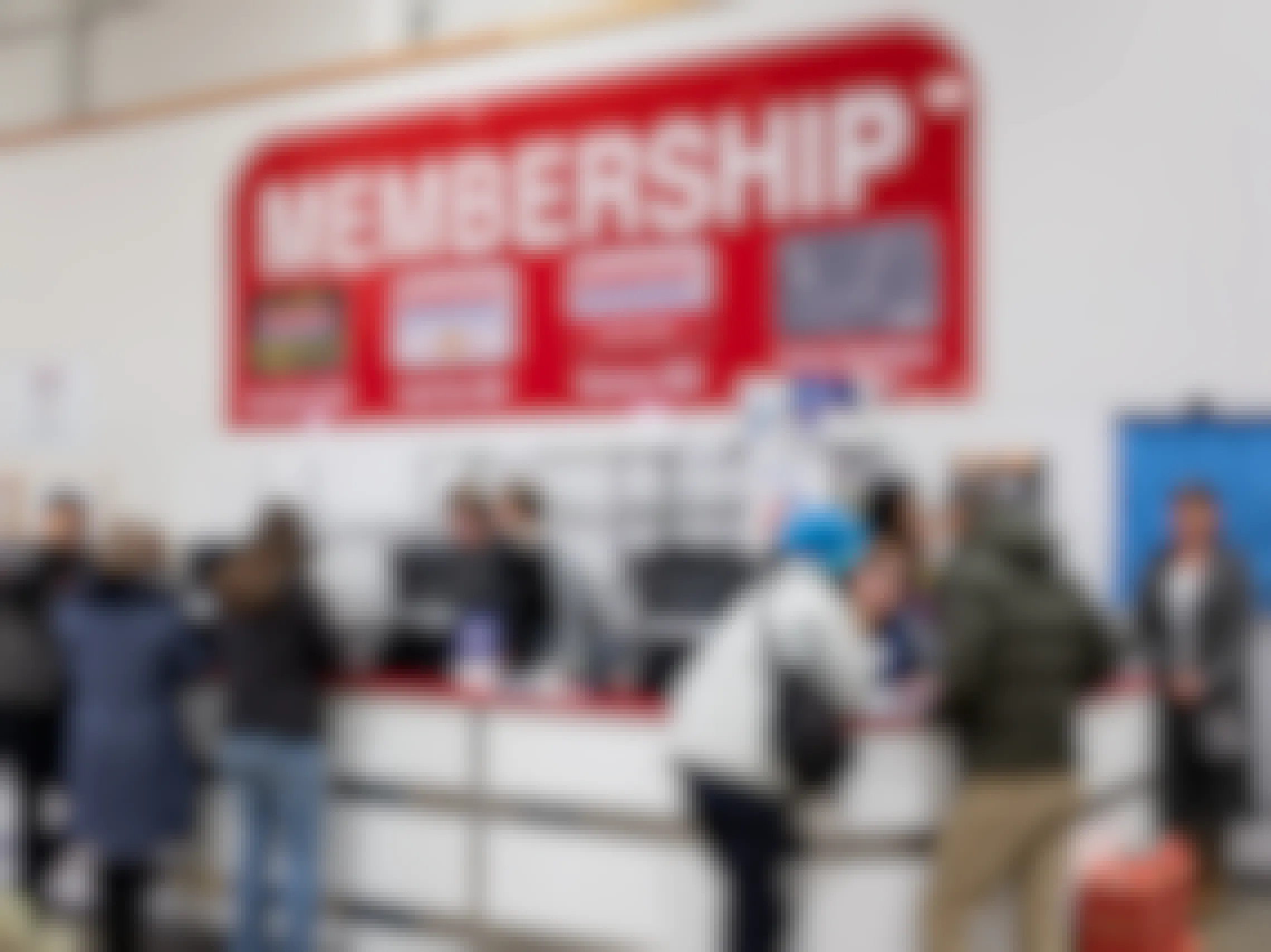 Costco customers standing at the Membership counter with a large sign listing the membership prices.