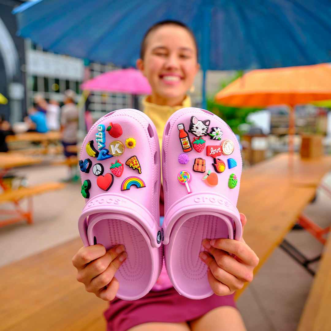 person holding pair of bubble gum pink crocs with multiple crocs charms on them