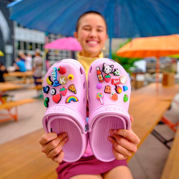 person holding pair of bubble gum pink crocs with multiple crocs charms on them