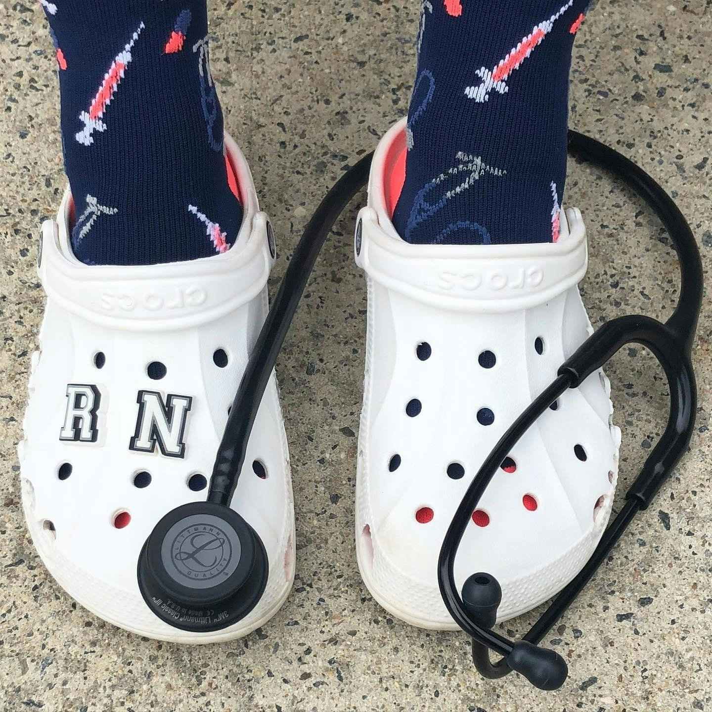white pair of crocs with the letters RN on them in jibbitz with a stethoscope around one let 