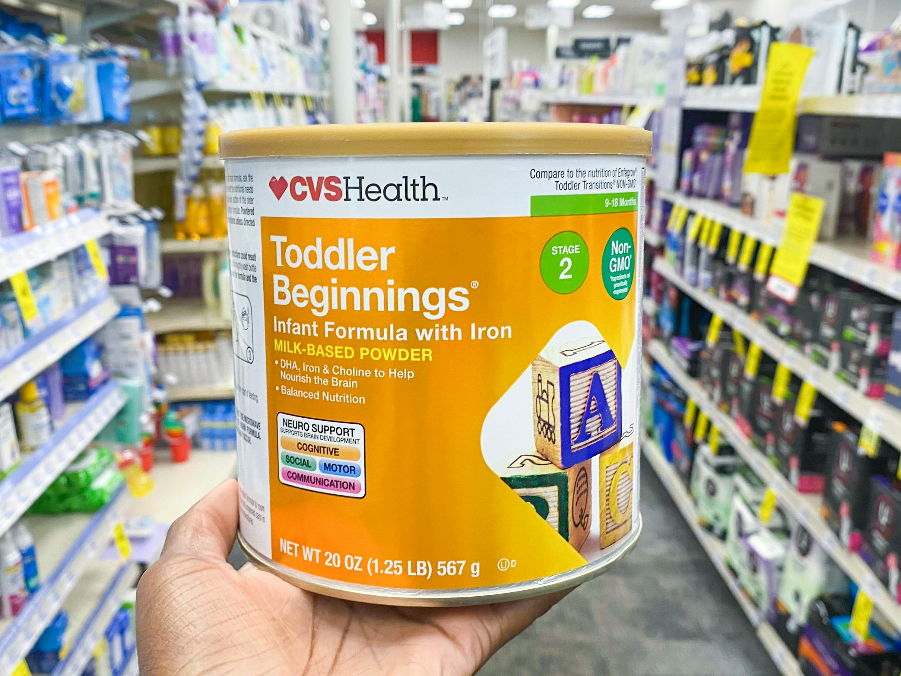 A person holding a container of CVS Health Toddler formula on an aisle inside CVS