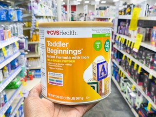 A person holding a container of CVS Health Toddler formula on an aisle inside CVS