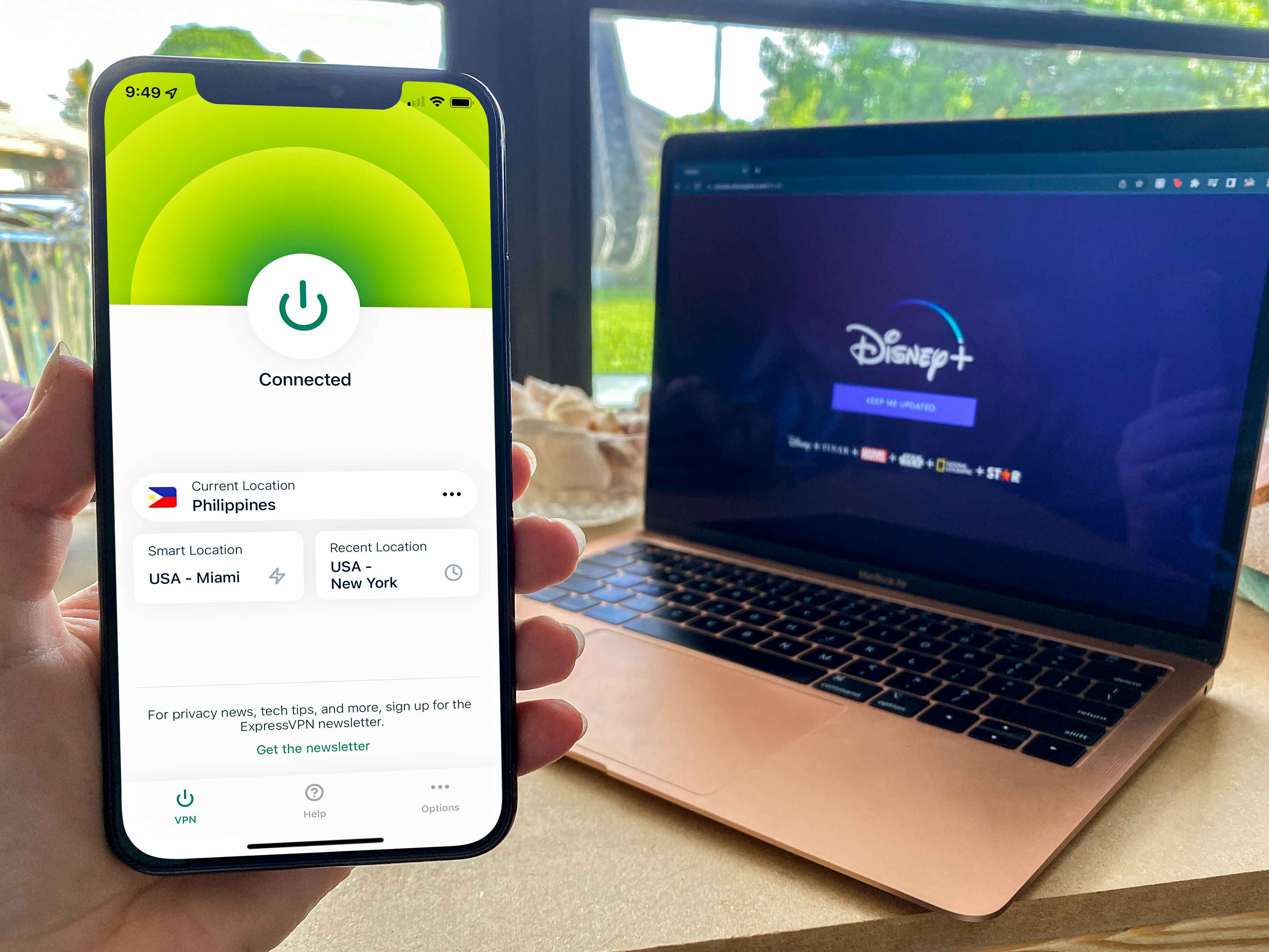 person holding phone with expressvpn screenshot next to laptop with disney plus