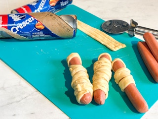 crescent roll dough and hot dogs on a cutting board ready to be baked into hot dog mummy snacks