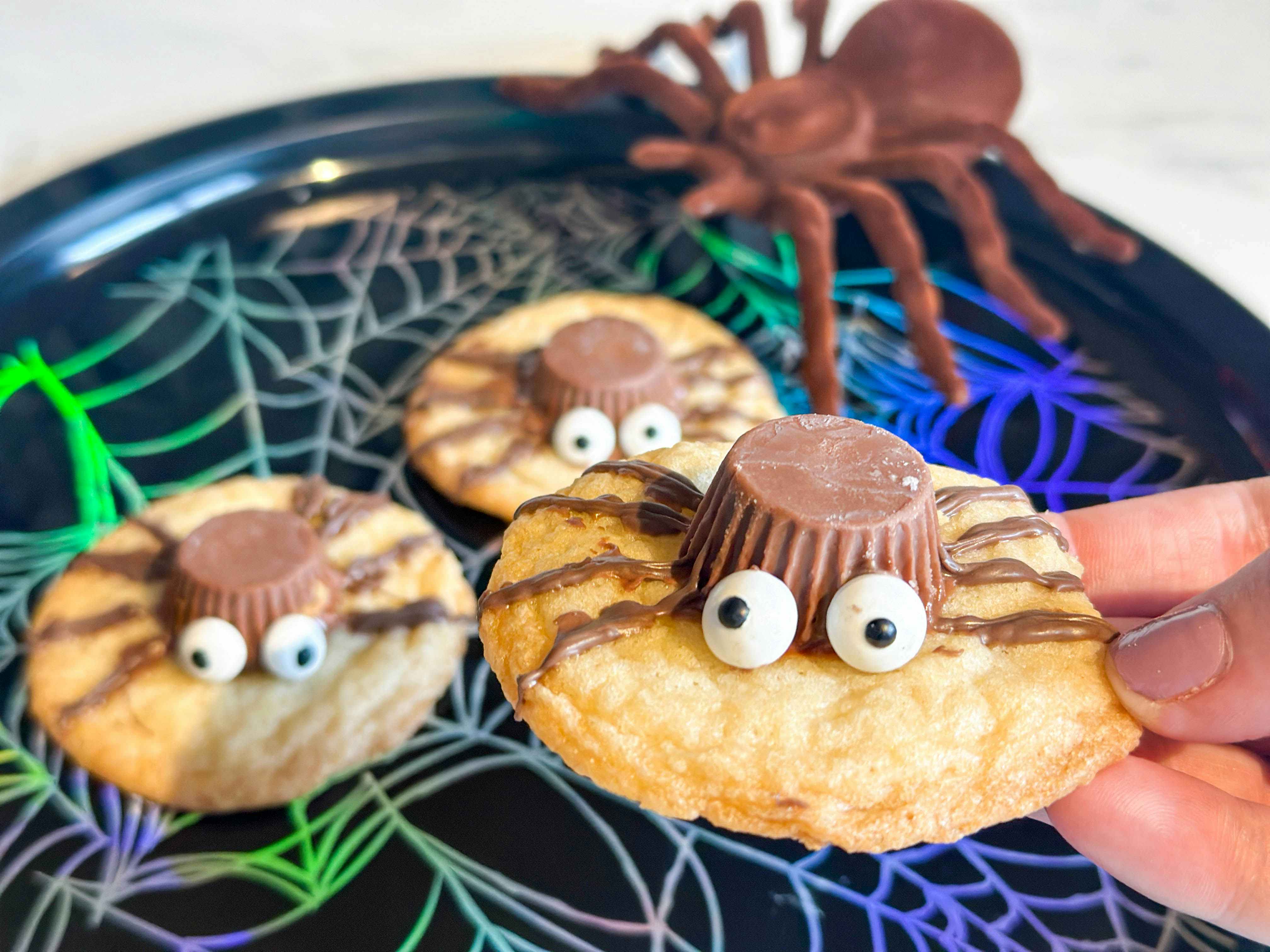 diy spider cookies being held up above a plate 