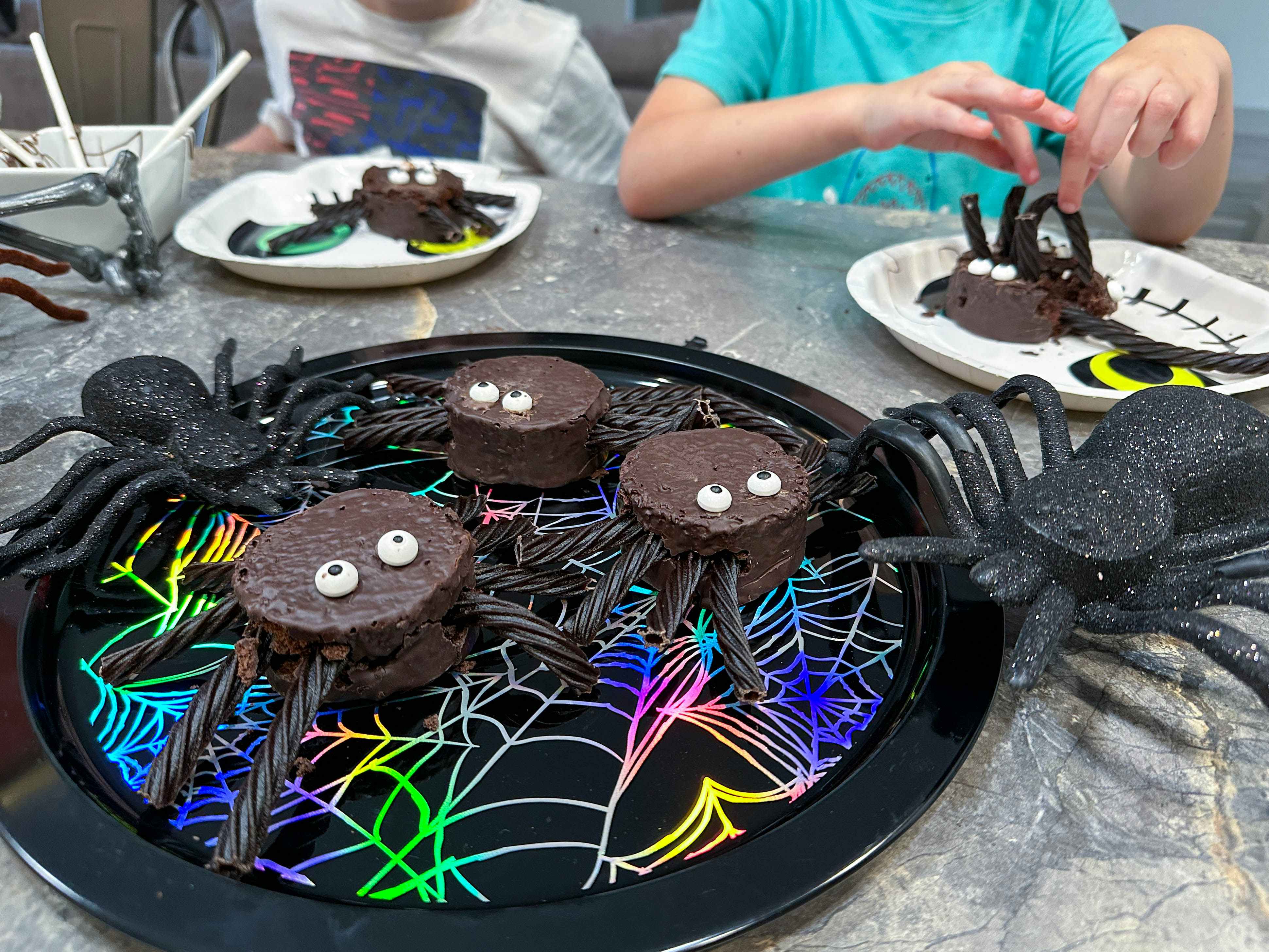 spider cakes on a tray with kids in the background making their own 