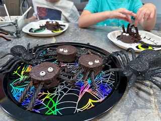 spider cakes on a tray with kids in the background making their own