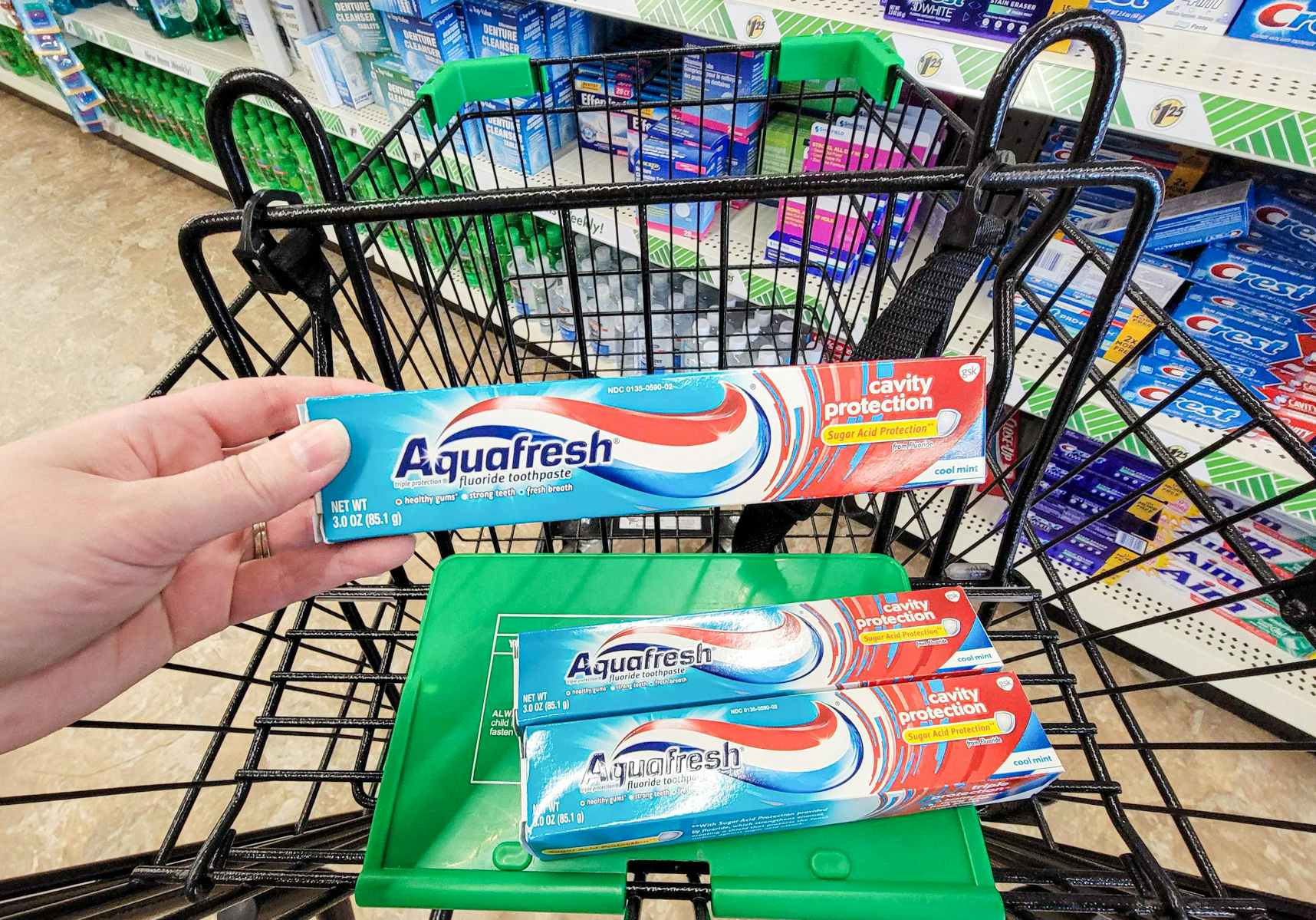 hand holding a tube of aquafresh toothpaste over the cart with 2 more tubes of aquafresh toothpaste in it
