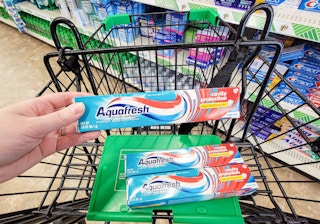 hand holding a tube of aquafresh toothpaste over the cart with 2 more tubes of aquafresh toothpaste in it