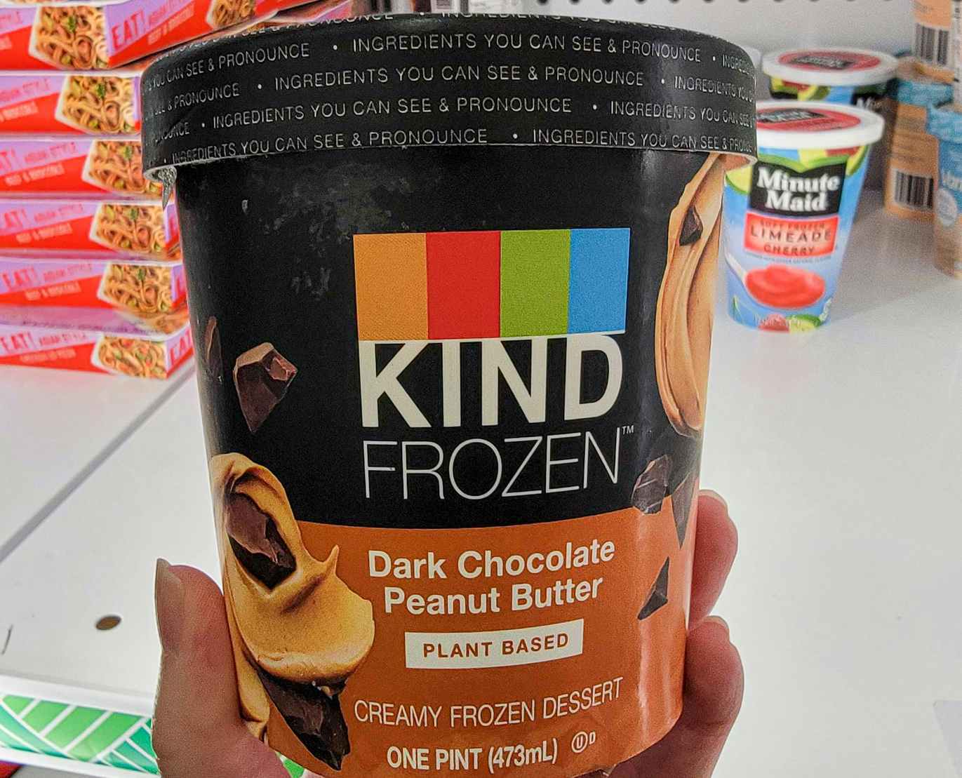 hand holding a container of kind frozen dessert in dark chocolate peanut butter flavor