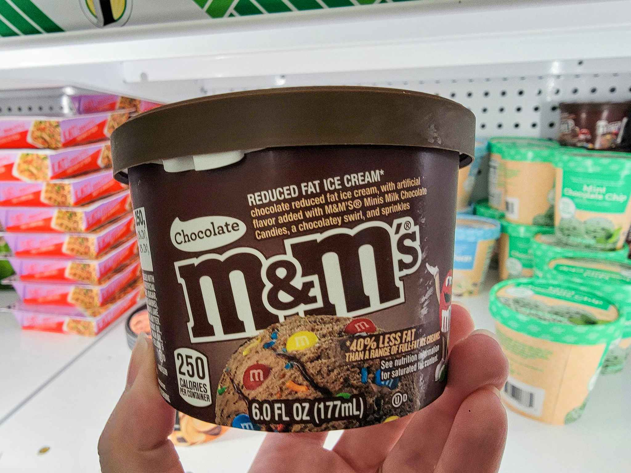 hand holding a tub of chocolate m&ms ice cream