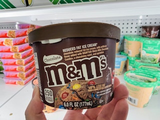 hand holding a tub of chocolate m&ms ice cream