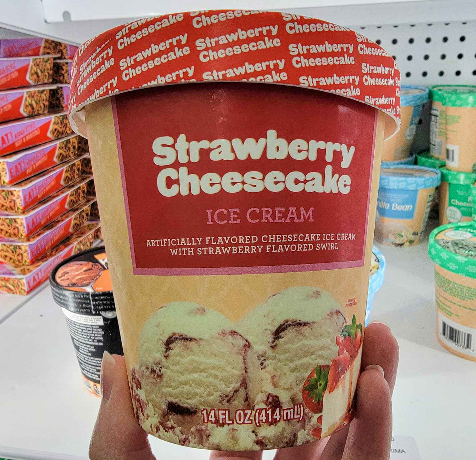 hand holding a tub of strawberry cheesecake ice cream