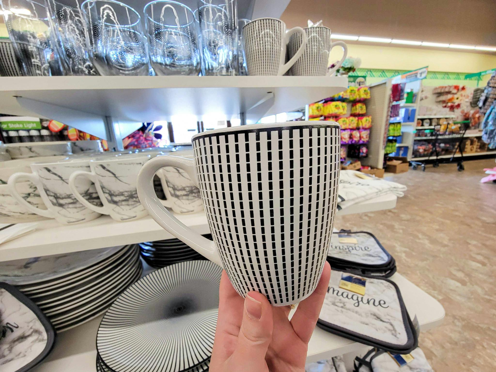 hand holding a white coffee mug with short black lines all over it forming a pattern