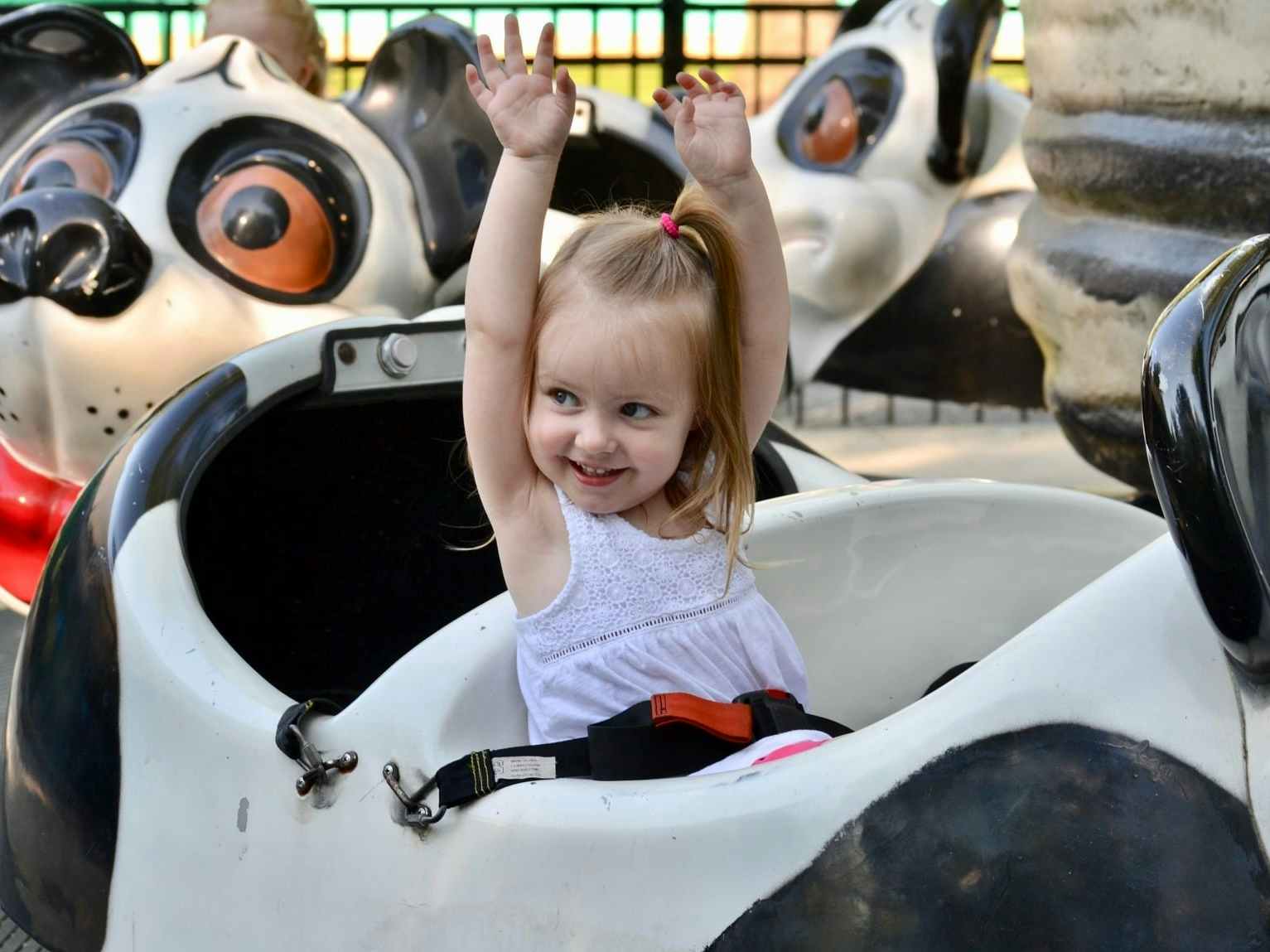 A little girl riding a ride at Dutch Wonderland with her arms up in the air.
