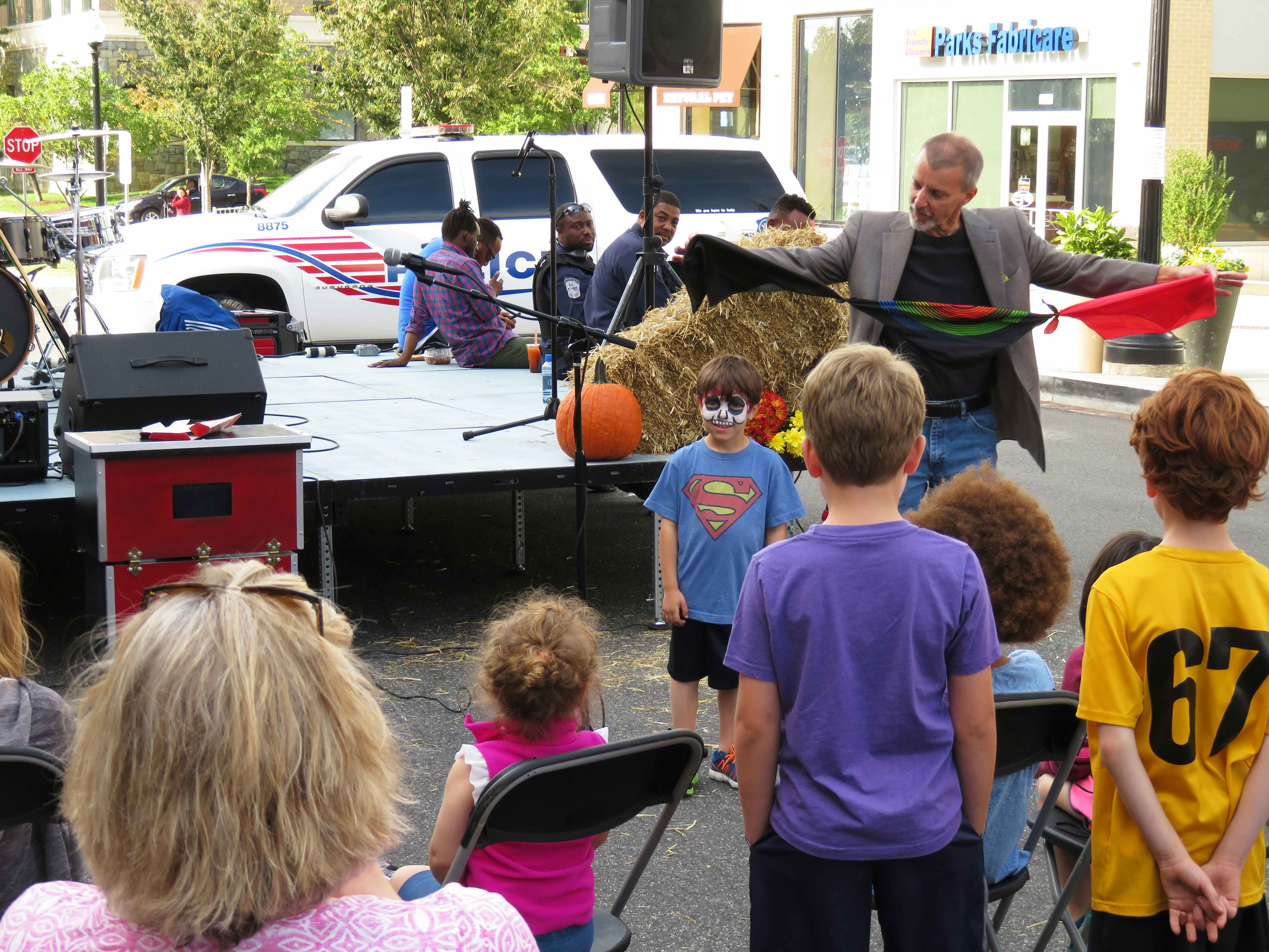 A magician performing a magic trick at a fall festival with children watching.
