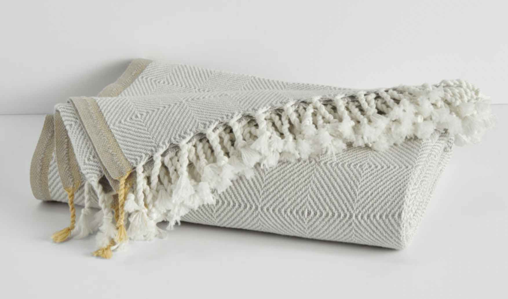 a cotton cashmere throw rolled up with fringe on the edges