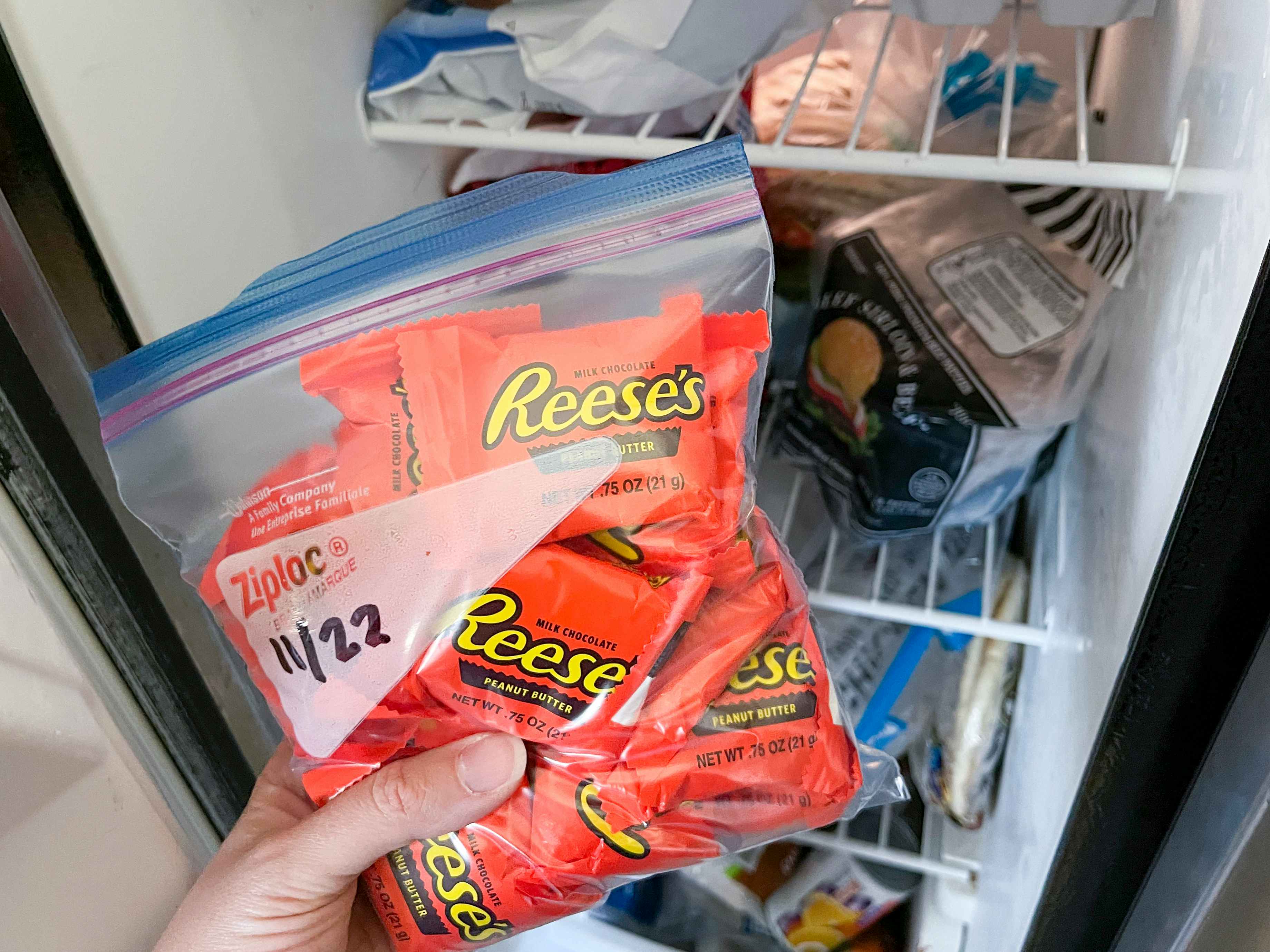 A person putting a Ziploc bag of leftover Halloween candy into their freezer.