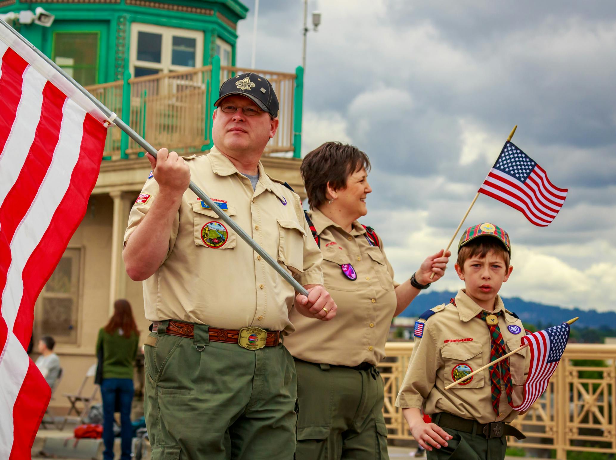 A boy scout troop and leader walking in a parade with American flags.