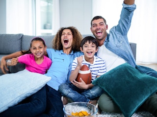 young family sitting on couch watching football