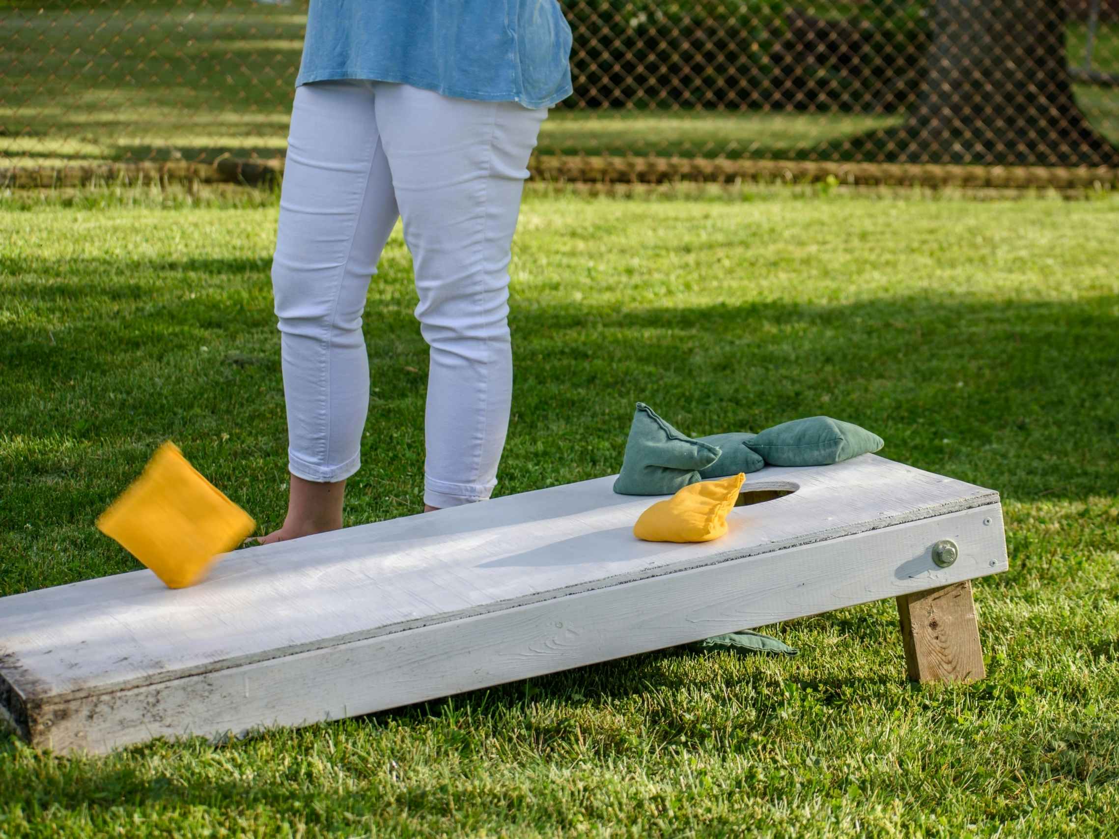 A person standing next to a cornhole board that has bean bags being tossed at it.