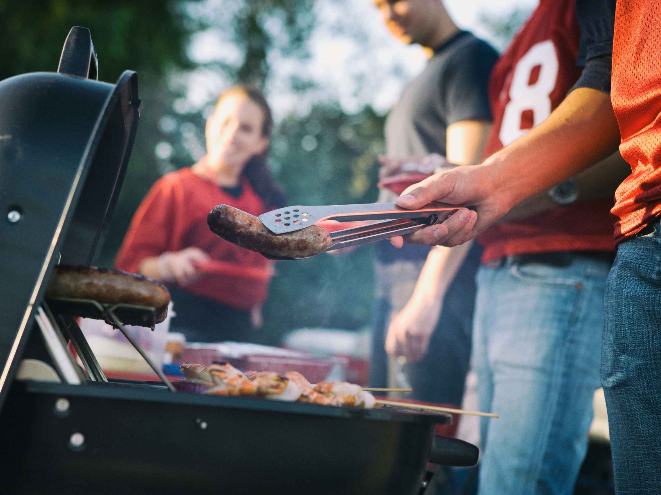 A close up on someone grilling some sausages on a grill at a tailgate party.