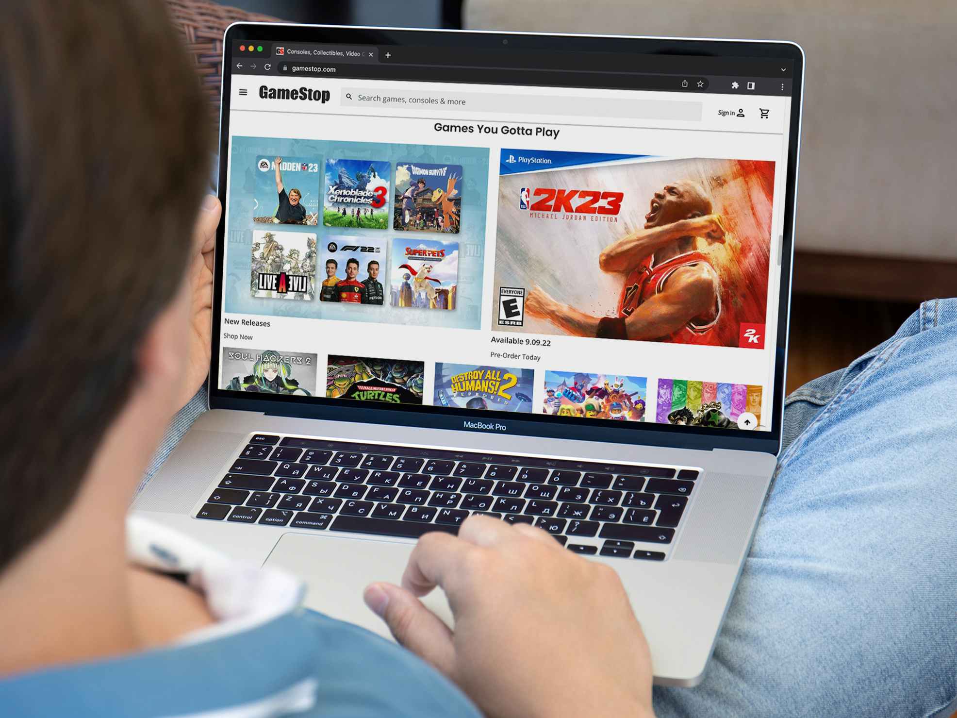 A person using a laptop displaying GameStop's website.