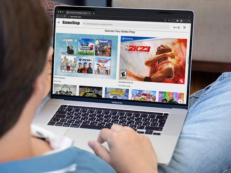 A person using a laptop displaying GameStop's website.