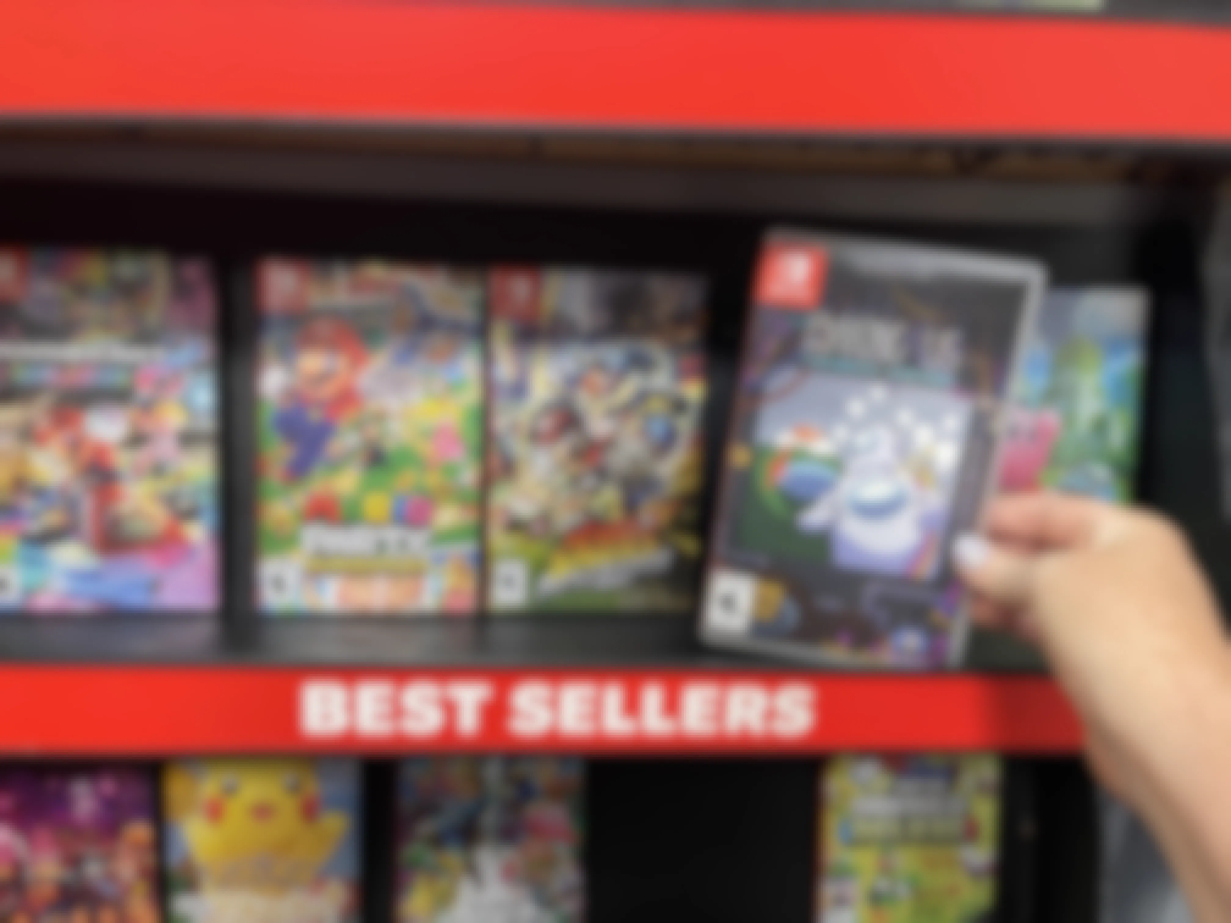 A person's hand taking an Among Us game off of a Best Sellers shelf at GameStop.
