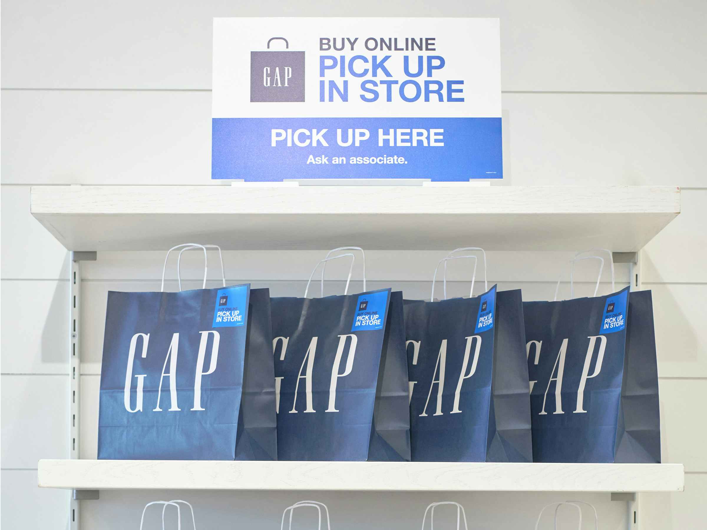 A shelf filled with in-store pick up bags, under a sign that reads gap pick up in store.