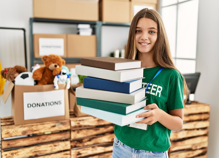 girl in volunteer shirt holding books donations