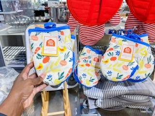 someone holding oven mitts with veggies and chickens on it