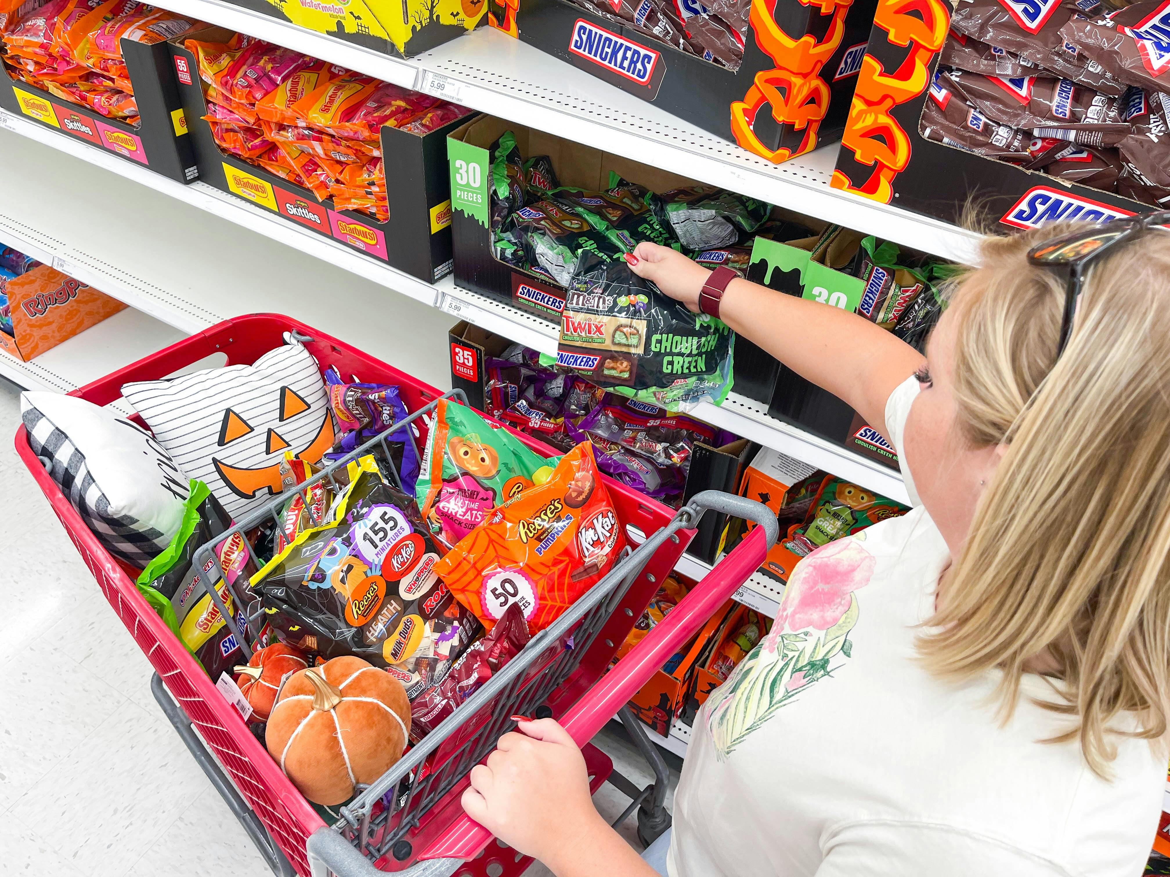 A woman shopping for Halloween candy in Target with a shopping cart full of Halloween items.