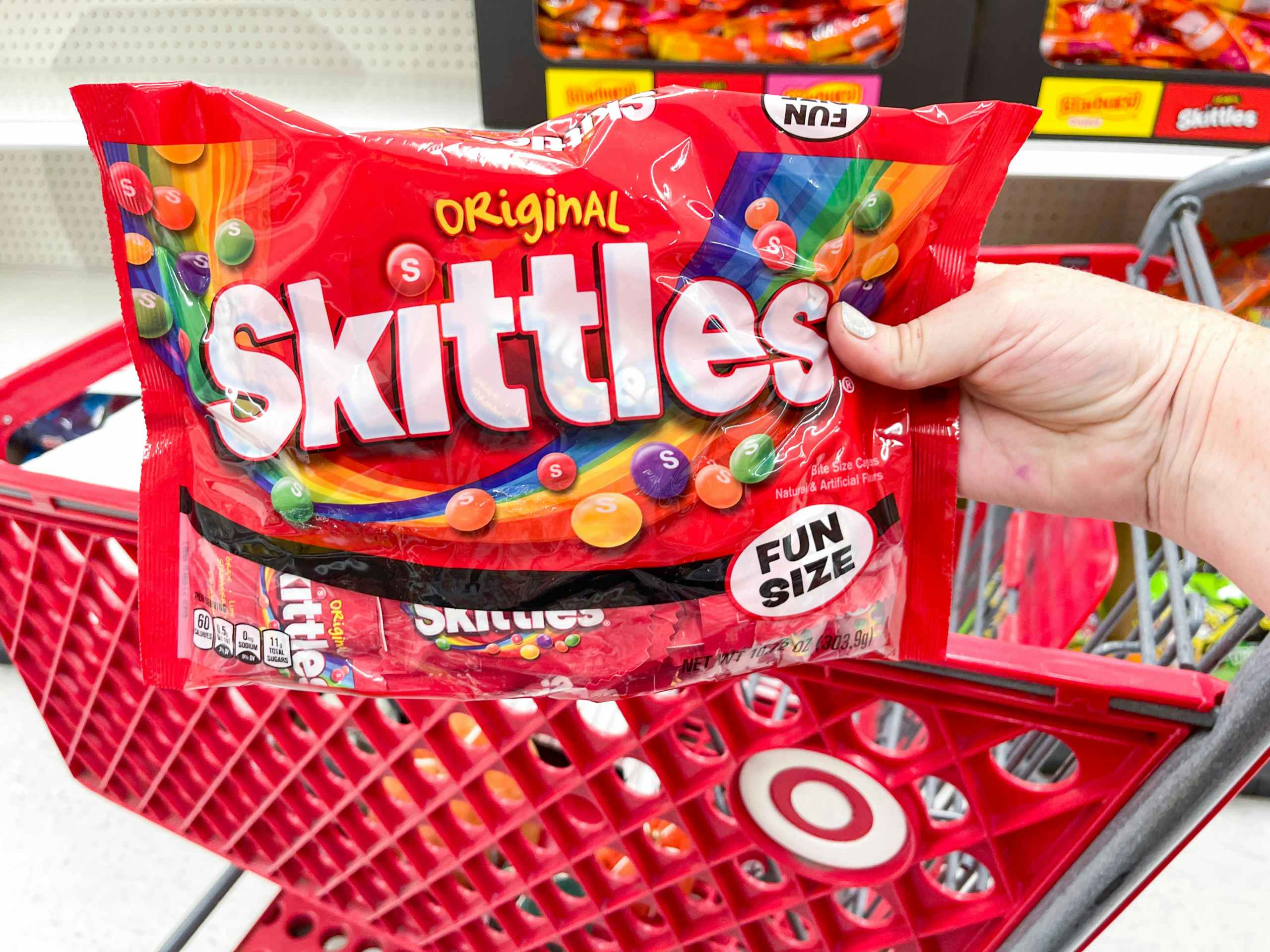 a person holding skittles in store by cart